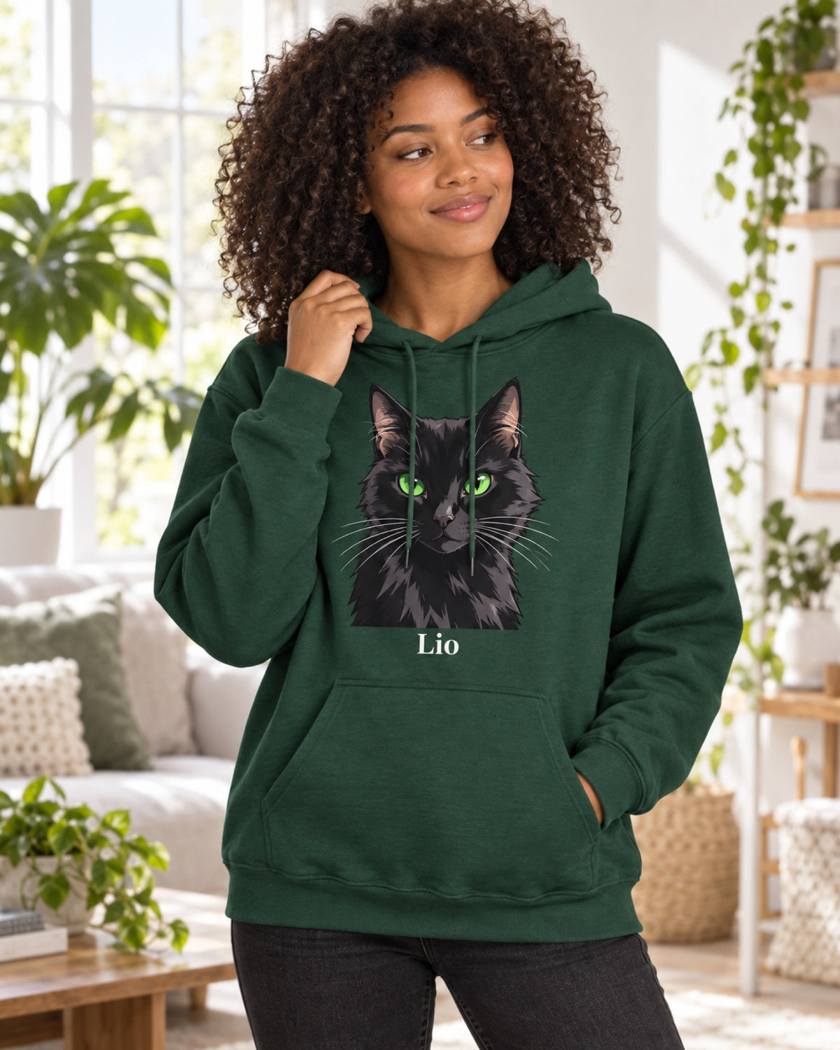 Flaschengrüner Hoodie mit schwarzer Katze im Cartoon-Stil und Namen Lio, eine Frau steht im hellen Wohnzimmer