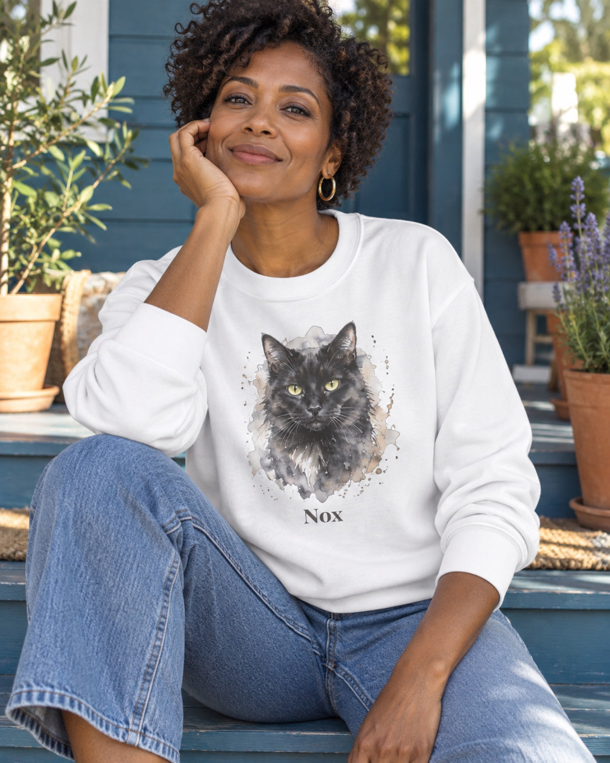 Frau im weißen Sweatshirt mit schwarzer Katze Nox als Portrait auf einer meerblauen Veranda