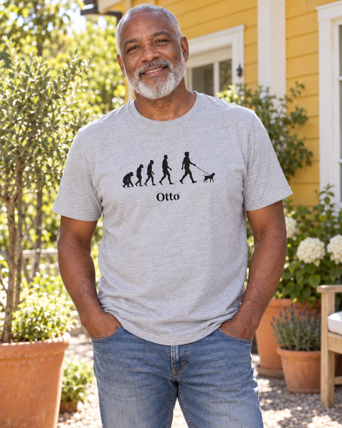Mann im graumelierten Pet Evolution T-Shirt mit Beispielname Otto vor einem gelben Gartenhaus