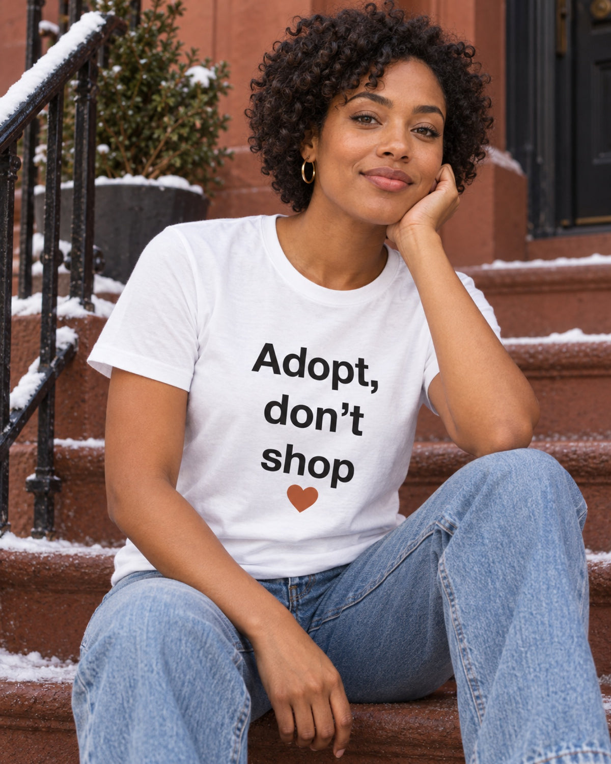 Frau im weißen T-Shirt mit festem Adopt, don't shop Motiv und Herz an einem rostroten Wintertreppenabsatz